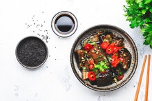 Grilled Spicy Eggplant With Hot Red Chili Peppers, Soy Sauce, Garlic And Sesame Seeds In Asian Style, White Table Background, Top View