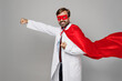 Side view male doctor man wear white medical gown suit work in hospital wear red super hero coat stand akimbo hands on waist isolated on plain grey color background studio Healthcare medicine concept