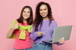 © ViDi Studio - Young two friends IT women in green purple shirts looking camera together hold use work point on laptop pc computer show thumb up isolated on pastel plain light pink color background studio portrait