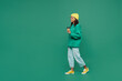 Full body side view little kid teen girl of African American ethnicity 13-14 year old wear casual hoody hat hold takeaway delivery craft paper cup coffee to go isolated on plain dark green background