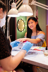 Wall Mural - young asian woman filing the nails during her manicure treatment at the beauty salon, wellness and hands care concept