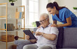 Nurse shows old man how to use apps on digital tablet to monitor his health and how to read e-books. Smiling pensioner looking at screen of modern device. Elderly people healthcare tech concept.