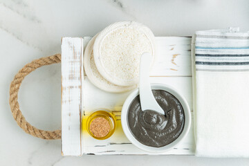 Poster - Organic cosmetic black clay, essential oil and lufa csponges on a white textured tray. The concept of spa and wellness. Top view.