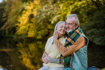 Wall Mural - Senior couple in love huging each other near lake, during autumn day.