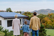 © Halfpoint - Rear view of family looking at their house with installed solar panels. Alternative energy, saving resources and sustainable lifestyle concept.