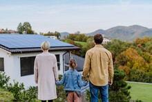 Rear View Of Family Looking At Their House With Installed Solar Panels. Alternative Energy, Saving Resources And Sustainable Lifestyle Concept.