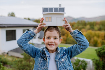 Wall Mural - Close up of happy little girl holding paper model of house with solar panels.Alternative energy, saving resources and sustainable lifestyle concept.