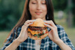 © MZaitsev - Young attractive hungry woman bites a big hamburger outdoor. Close up.