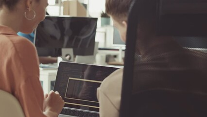 Couple of young programmers looking at laptop screen while discussing program coding at workplace