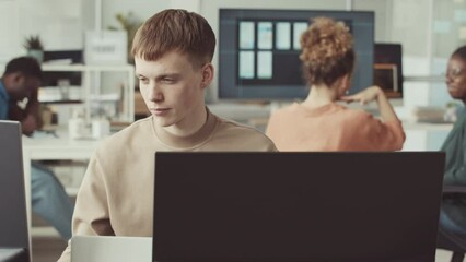 Young Caucasian male programmer looking at computer monitor while working in IT office with diverse colleagues