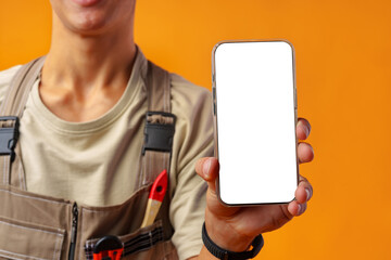 Wall Mural - Portrait of handyman in uniform showing blank mobile phone on yellow background