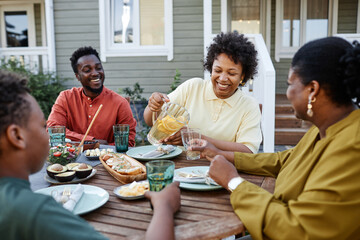 Wall Mural - Portrait of smiling black woman pouring lemonade drinks to glass during family gathering outdoors