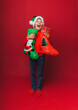 © inna717 - a boy in a knitted red sweater and a Santa Claus hat holds a Christmas boot for gifts. Cute baby is waiting for Christmas and a new kind. insulation on a red background.