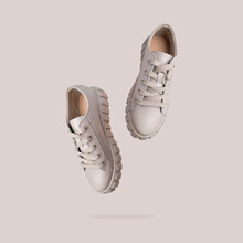 Beige Gray Leather Female Sneakers With Lace Isolated On Beige Background. Flying Fashion Stylish Casual Sneakers, Sports Unisex Clothing Shoes. Advertising Minimal Mockup With Footwear