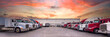 Lined up Semi trucks on a parking lot at logistics warehouse with orange sunset sky.