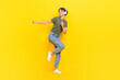 Full length photo of funny funky lady look empty space wear earbuds listen playlist enjoy sound isolated on yellow color background