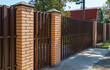 Brown metal fence with brick posts. Metal fencing of private property in the countryside. Security concept