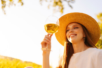 Wall Mural - close-up low-angle view of cheerful ginger young woman in straw hat holding wineglass on background 