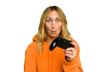 Wall Mural - Young caucasian gamer woman holding a game controller isolated on green chroma background shrugs shoulders and open eyes confused.