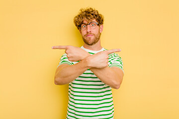 Wall Mural - Young caucasian man isolated on yellow background points sideways, is trying to choose between two options.