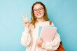 © Asier - Young student caucasian woman isolated on blue background joyful and carefree showing a peace symbol with fingers.
