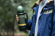 © Mihail - person holding a metal thermos with hot water outdoors