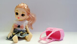 Fototapeta  - Lalka na szarym tle z porzuconą różową torebką