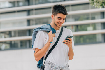 Wall Mural - young man walking in the street looking at the mobile or cell phone