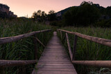 Fototapeta Zachód słońca - Scenic view of a wooden pier on a blue lake at dawn. Reflection of mountains and water plants on water in Una, Cuenca, Spain