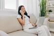 © SHOTPRIME STUDIO - Young Asian woman looking at laptop screen on her lap sitting on couch at home lifestyle work as a freelancer