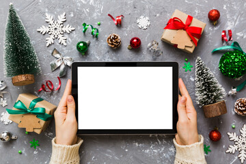 Wall Mural - Christmas online shopping from home, female hands holding tablet pc with blank white display top view. woman hand holding tablet with blank screen, Christmas tree and gifts on background