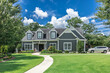 A large gray craftsman new construction house with a landscaped yard and leading pathway sidewalk