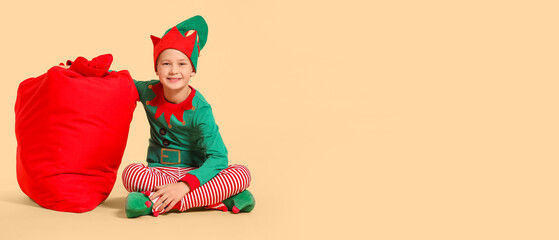 Canvas Print - Little boy in costume of elf and with Santa bag on beige background with space for text