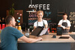 © Pixel-Shot - Young female barista showing menu to visitor in cafe