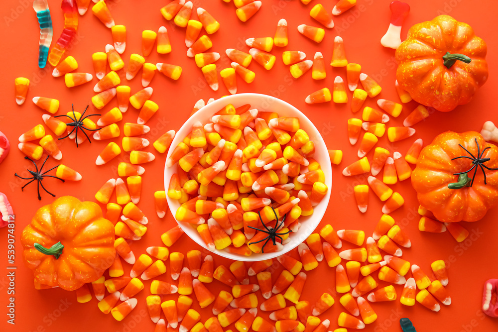 Bowl with Halloween candies and pumpkins on red background