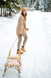 Happy woman with sledge walking among winter forest