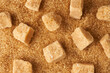 Trzcinowy  cukier w kostkach porozrzucany na rozsypanym brązowym cukrze