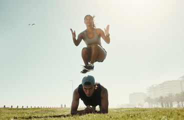 Canvas Print - Energy, training and intense couple workout in a park with serious, cool and wellness in nature. Cross, different and fit jumping woman with man doing ground pushup in extreme physical exercise