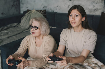 Two women senior mother and daughter playing video game sitting on the floor in the bedroom. Happy family. Fun play together. Having fun and enjoying time