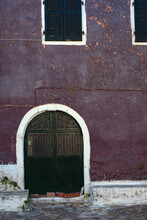 Weathered Purple Building With Dark Green Door And Closed Shutters.