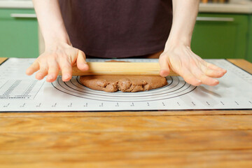 Wall Mural - Rolling out gingerbread dough on a silicone baking mat on a wooden table with copy space.