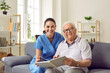 © Studio Romantic - Senior man enjoying quiet pastime in retirement home. Portrait of nurse together with eledrly patient. Happy old male patient and young female nurse sitting on sofa and reading book together