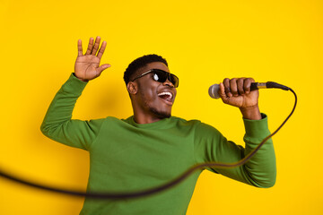 Wall Mural - Portrait of handsome trendy cheerful guy having fun singing single pop isolated over bright yellow color background