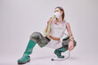Portrait of young beautiful girl in rubber boots, vacuum cleaner on back and mask isolated on grey background. Fresh air