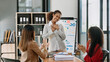 © Nuttapong punna - Mid age Asian business woman ceo executive manager showing to colleagues team income revenue data figures planning on big screen in office.
