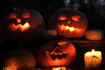 Wall Mural - Halloween Pumpkin Head with Carved Scary Smiling Face at Night Outside. Jack-O-Lantern, Burning Candles Outdoor. Halloween Dark Composition Backyard Decor. Pumpkins Black Background. All Saints Day 4K