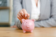 © dragonstock - Businesswoman putting money into piggy bank. Concept of money saving and budgeting. Saving money with pink cute piggy bank