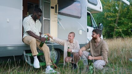 Poster - Student camping party. Multiracial friends sitting outside of their camper with tasty beer in green glass bottles, sharing a salty snack. Van life. High quality 4k footage