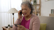 © PRPicturesProduction - half length shot of a asian grey haired senior woman giving credit card details on the mobile phone in the living room at home