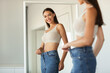 © Prostock-studio - Lady Wearing Jeans After Slimming Comparing Size Near Mirror Indoors